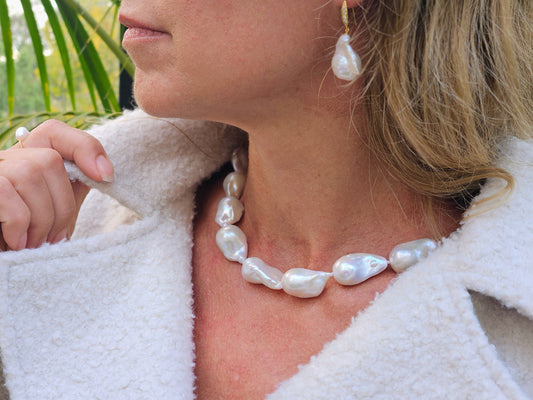 a close up of a woman wearing a fuzzy white jacket and baroque pearl necklace and earrings